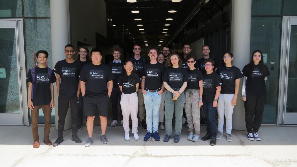 a number of people standing in front of a building all wearing the same black Wright Lab t-shirt.
